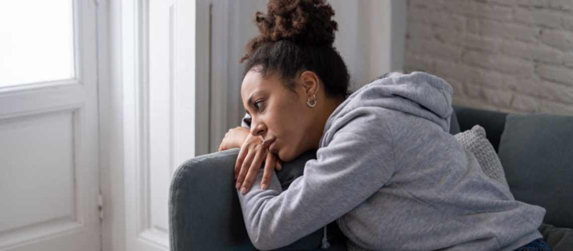 Lonely young afro latina young woman on sofa feeling in pain, exhaustion and sadness. Depressed hispanic or afro american girl at home, looking away with sad expression. In Mental health concept.
